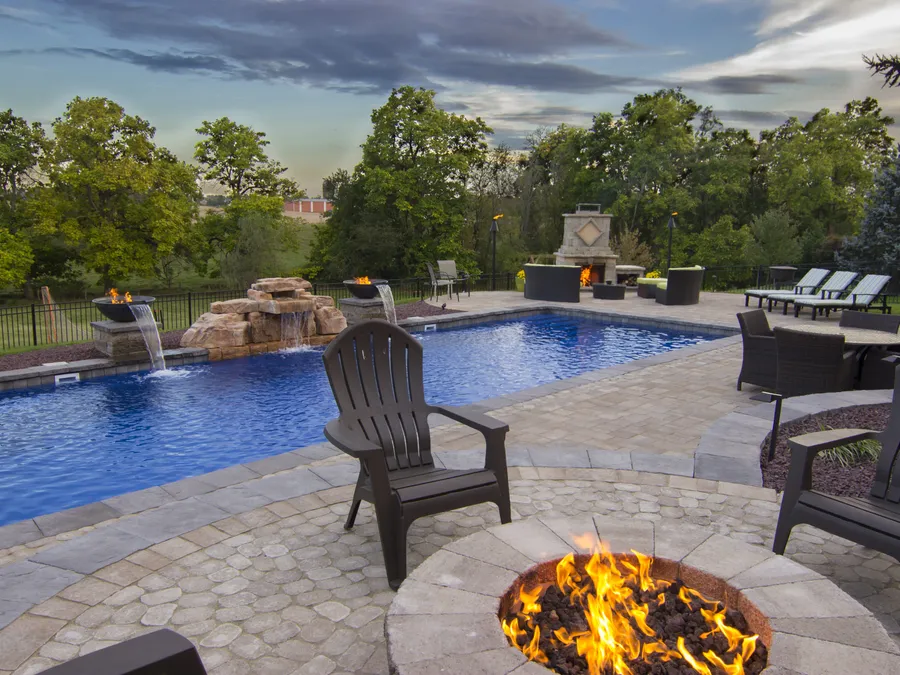 A round paver fire pit burning on an HPC Fire insert beside a pool