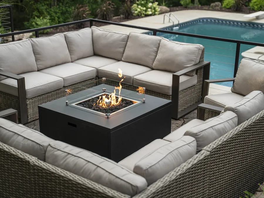 A Stoll square fire table inside a wicker sectional beside a pool