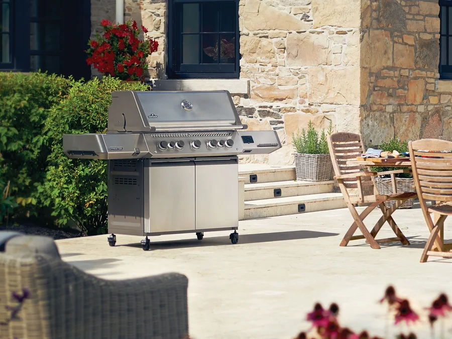 A Napoleon Prestige cart grill on a stone patio beside a dining table