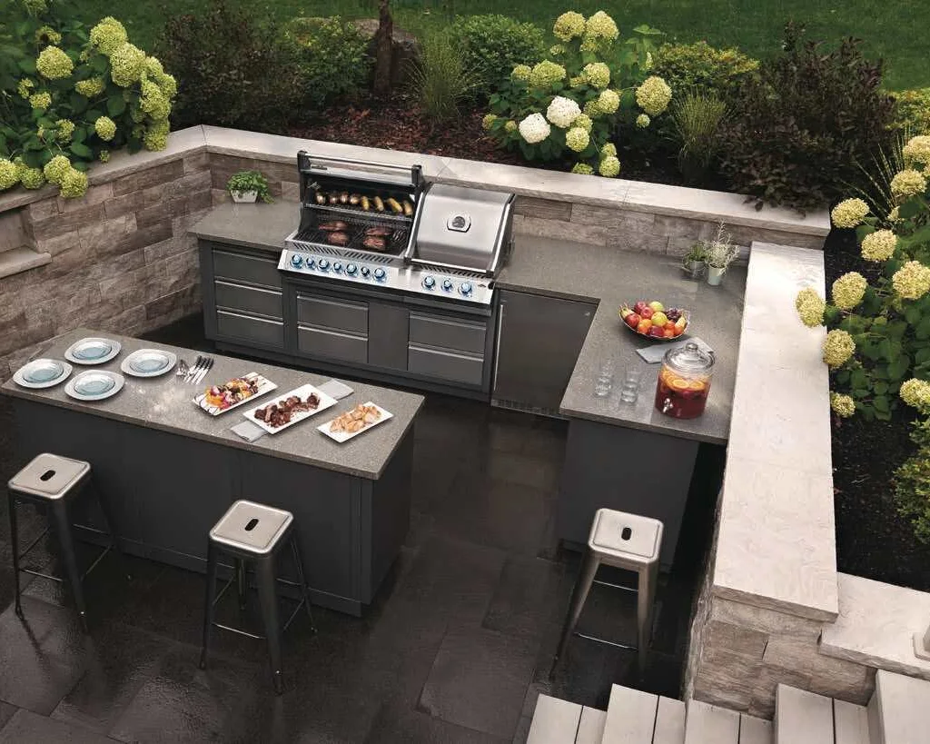 A Napoleon built-in grill in a stone outdoor kitchen with an island and stools