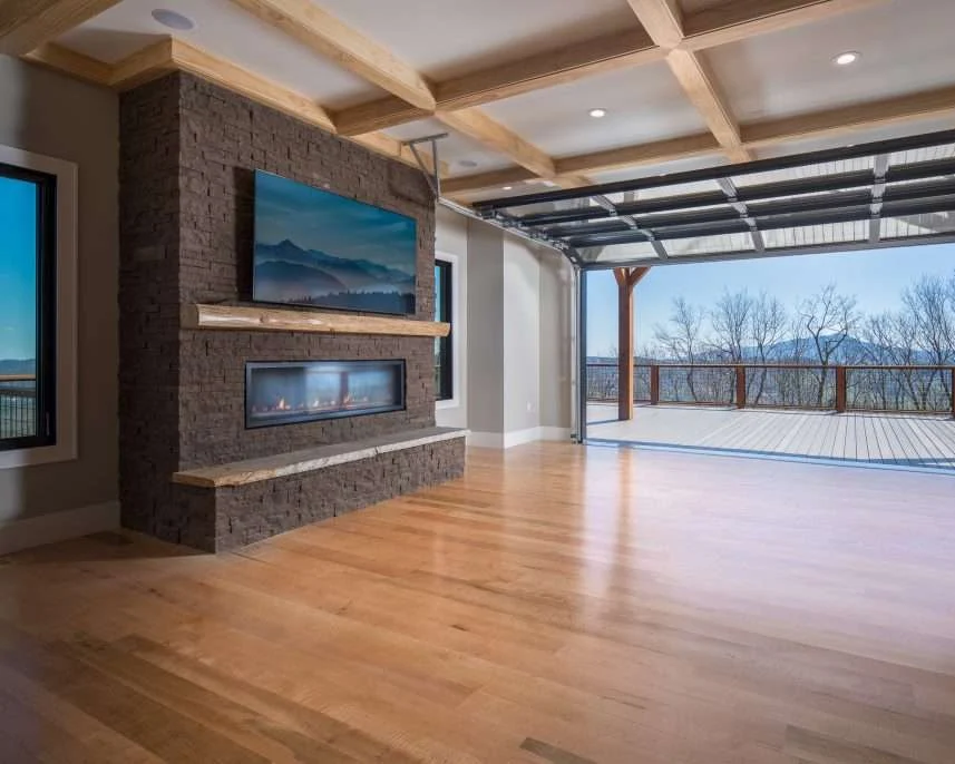 A dark Evolve Stone fireplace wall with a linear fireplace and a live-edge mantel in a great room that opens to a deck
